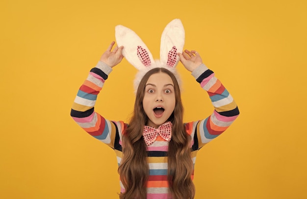 Amazed easter child in bunny ears and bow tie on yellow background