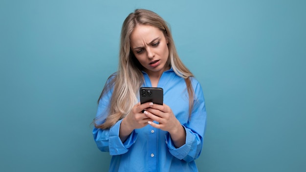 Amazed enchanted blonde woman holding a phone in her hands on a blue bright background