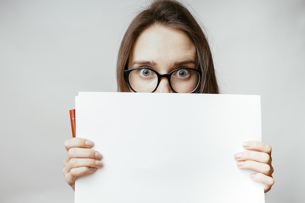 Amazed face woman hide behind paper, a frightened girl peeks out from behind a sheet of A4