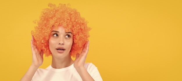 Amazed fancy party look freaky woman in clown wig on yellow background express positive emotions