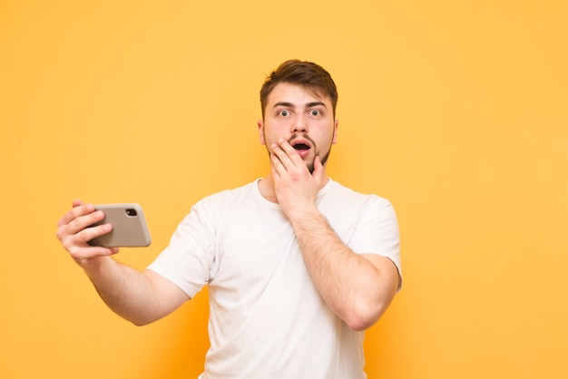 Amazed gamer with a smartphone in his hands isolated on yellow