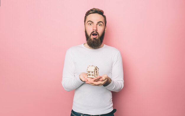 Amazed guy is standing and holding a wood toy house