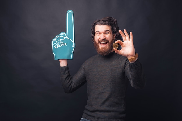 Amazed handsome bearded man showing bitcoin and pointing with fan glove