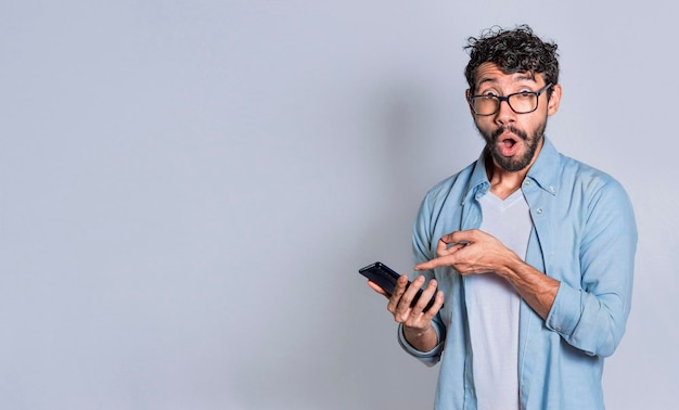 Amazed handsome man pointing at his cell phone isolated surprised person pointing at his cell phone isolated Isolated teenager surprised of a promotion on his cell phone