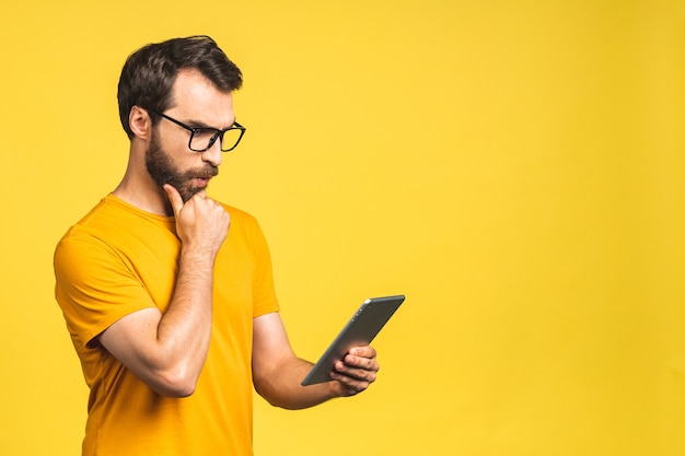 Amazed happy bearded man using digital tablet looking shocked about social media news, astonished man shopper consumer surprised excited by online win isolated over yellow background.