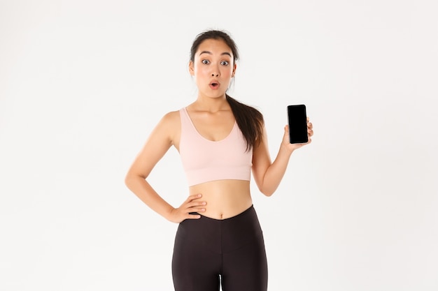   Amazed and impressed asian sportswoman, athlete say wow look thrilled and showing mobile phone fitness application, workout tracker app.