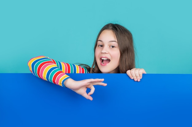 Amazed kid behind blank blue paper with copy space for advertisement ok