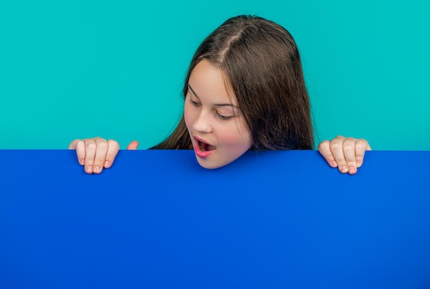 Photo amazed kid behind blank blue paper with copy space for advertisement