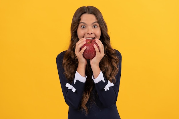 Amazed kid eating red vitamin apple for lunch on yellow background vitamin