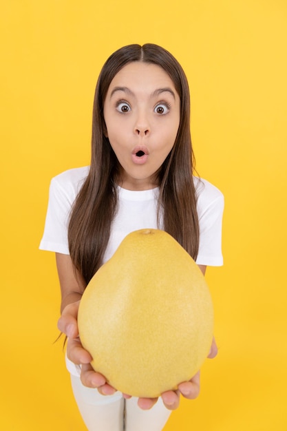 Amazed kid girl hold big citrus fruit of yellow pummelo or pomelo full of vitamin, selective focus, surprise.