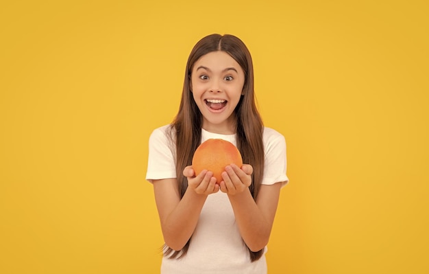 Amazed kid hold grapefruit on yellow background health