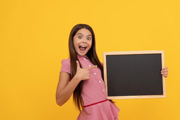 Amazed kid hold school blackboard for copy space showing thumb up announcement