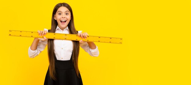 Amazed kid in school uniform hold mathematics ruler for measuring education banner of school girl student schoolgirl pupil portrait with copy space