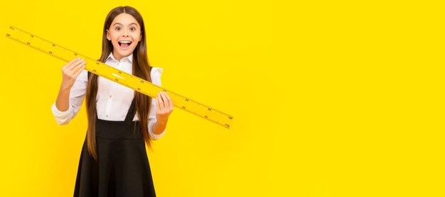 Photo amazed kid in school uniform hold mathematics ruler for measuring portrait of schoolgirl student studio banner header school child face copyspace