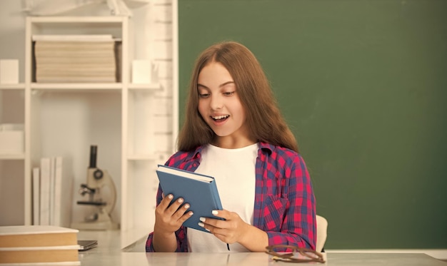 Amazed kid sitting with copybook in classroom at blackboard education