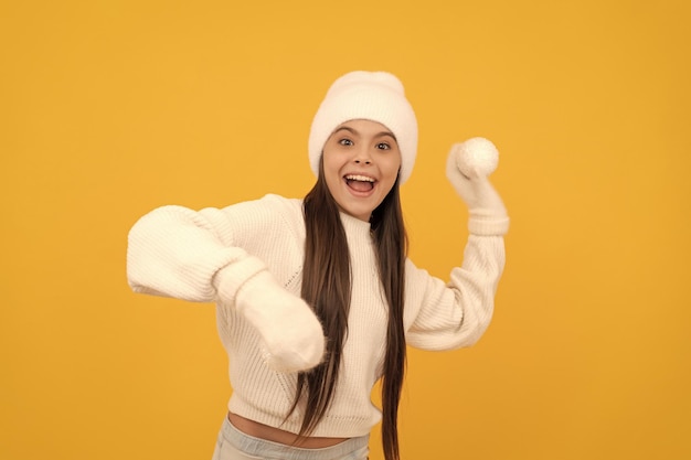 冬の帽子と手袋で驚いた子供は、黄色の背景の冬に雪玉で遊ぶ