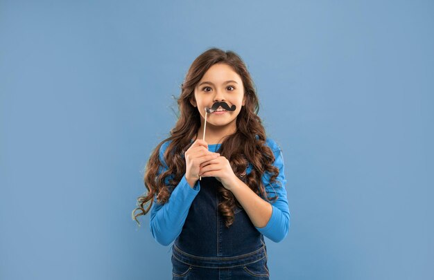 Amazed kid with curly hair hold party accessory of moustache party