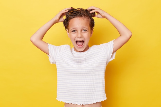 Photo amazed little girl with wet hair wearing casual white tshirt standing isolated over yellow background washing hair screaming with excitement