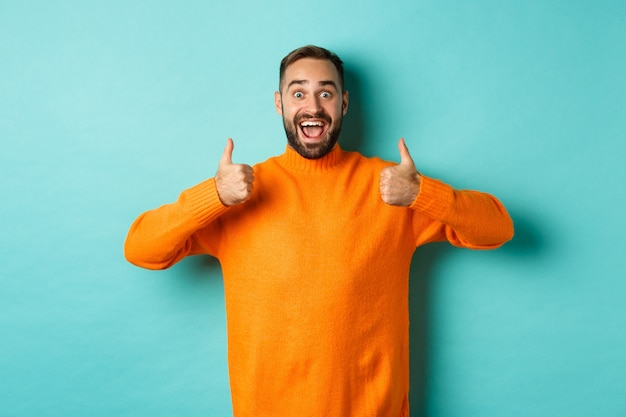 Photo amazed man showing thumbs-up, approve and praise something awesome, cool thing, standing over light