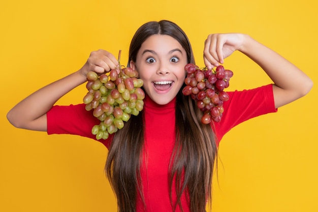 Amazed positive girl hold bunch of grapes on yellow background