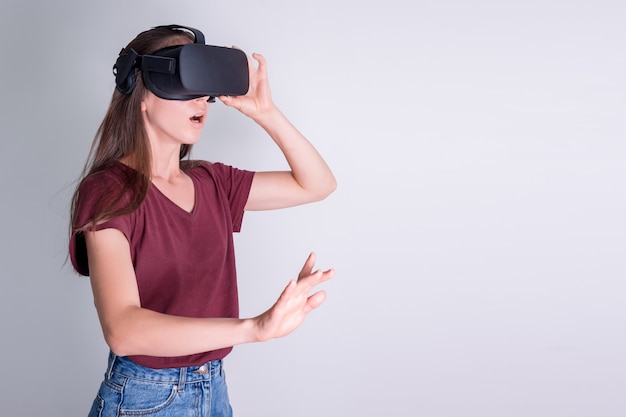 Amazed positive woman wearing virtual reality goggles headset, vr box. Connection, technology, new generation, progress concept. Girl surprised by something in virtual reality. Studio shot on gray