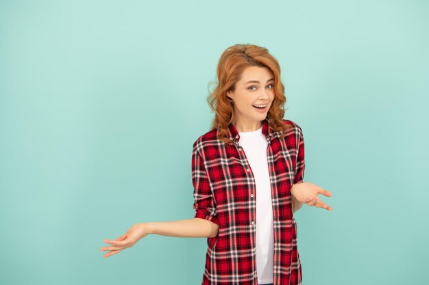 Amazed redhead woman in checkered shirt on blue background with copy space