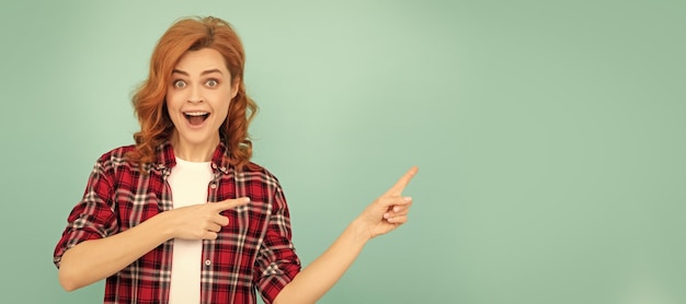 Photo amazed redhead woman in checkered shirt point finger on blue background woman isolated face portrait banner with mock up copyspace