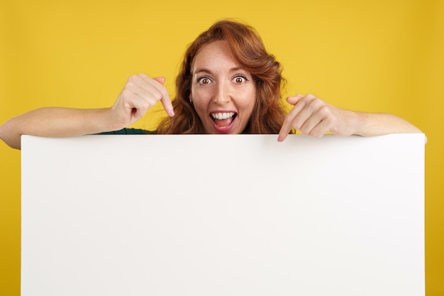 Amazed redheaded woman pointing to a panel with blank space