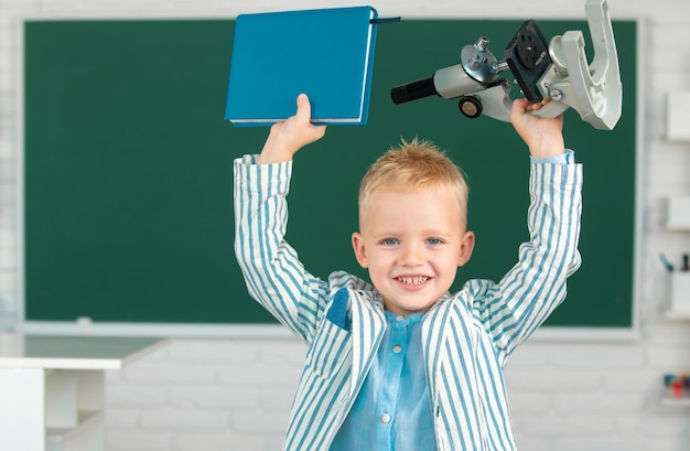 Amazed school boy with microscope and book child at school kid is learning in class on background of