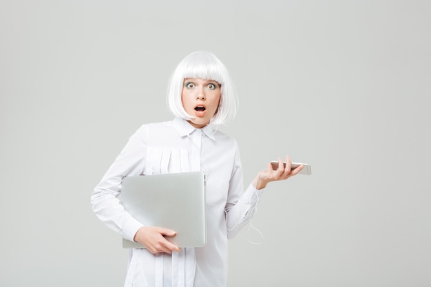 Amazed shocked young woman holding laptop and cell phone