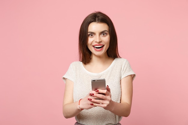 Amazed smiling young woman in casual light clothes posing isolated on pastel pink wall background studio portrait. people lifestyle concept. mock up copy space. using mobile phone, typing sms message