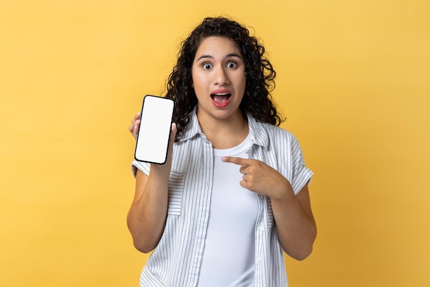 Amazed surprised woman holding pointing ar mobile phone with blank screen mockup for advertisement