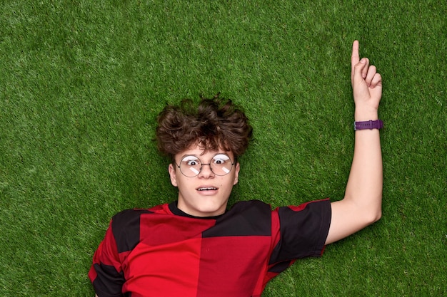 Amazed teen boy pointing up on grass