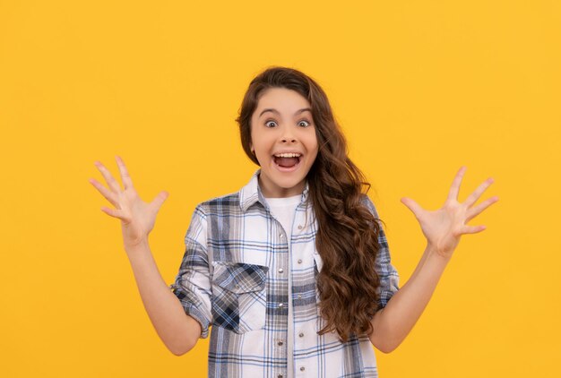 Amazed teen child in checkered shirt with long curly hair on yellow background