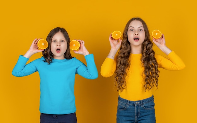 Amazed teen children hold orange fruit on yellow background