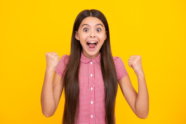 Amazed teen girl Excited expression cheerful and glad Teenager child doing winner gesture celebrate clenching say yes isolated on yellow background studio portrait