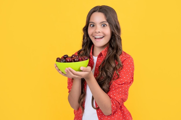 Amazed teen girl hold cherry bowl on yellow background