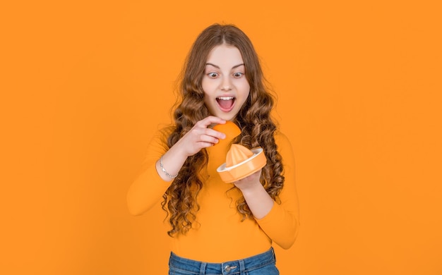 Amazed teen girl hold orange and juicer on yellow background