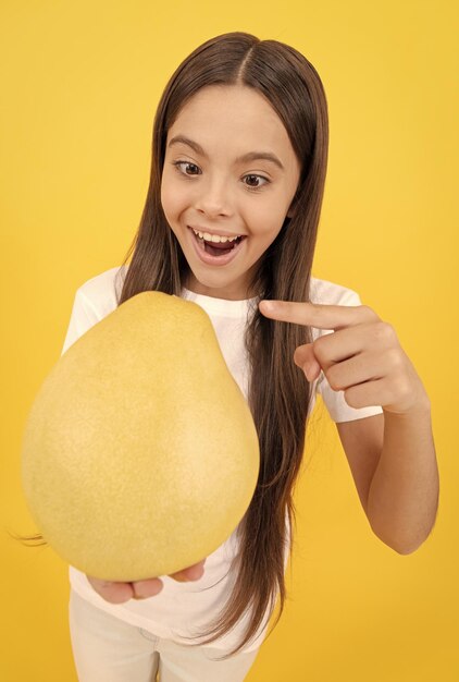 Amazed teen girl pointing finger on big citrus fruit of yellow pomelo full of vitamin selective focus exotic fruit