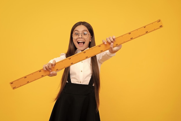 Amazed teen girl in school uniform and glasses hold mathematics ruler for measuring trigonometry