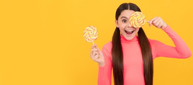 Amazed teen girl with lollipop candy on stick on yellow background Teenager child with sweets poster banner header copy space