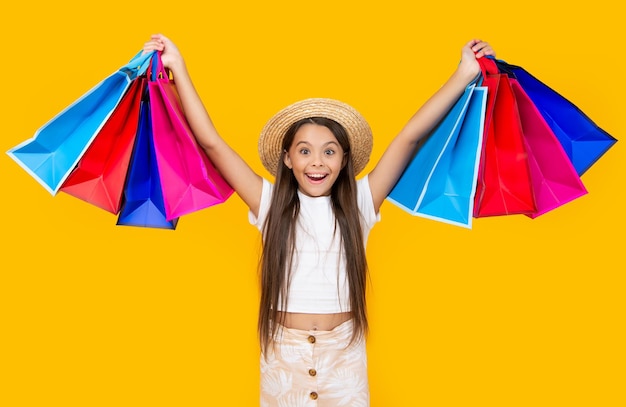Amazed teen girl with shopping bags on yellow background
