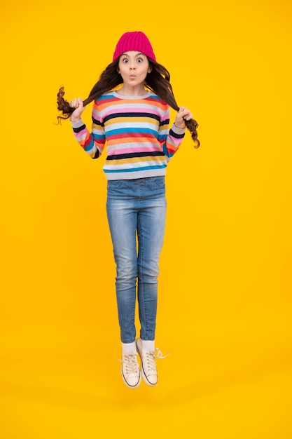 Amazed teenager Modern teen girl wearing sweater and knitted hat on isolated yellow background Excited teen girl Jump and run