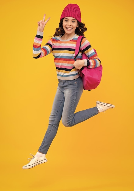 Amazed teenager schoolgirl child student with backpack and warn hat isolated yellow background learning and knowledge education concept crazy jump and run jumping kids excited teen girl