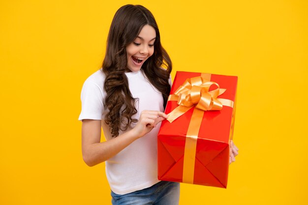 Amazed teenager teenager child holding gift box on yellow isolated background gift for kids birthday christmas or new year present box excited teen girl