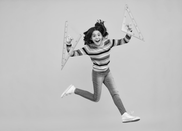 Удивленный подросток Подросток школьница держит меру для урока геометрии Измерение высоты Измерение оборудования Сумасшедшие прыжки прыгающие дети День знаний Возбужденная подростка школьница