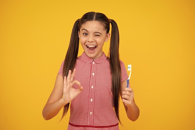 Amazed teenager teenager girl brushing her teeth over isolated yellow background daily hygiene teen child hold toothbrush morning routine dental health oral care excited teen girl