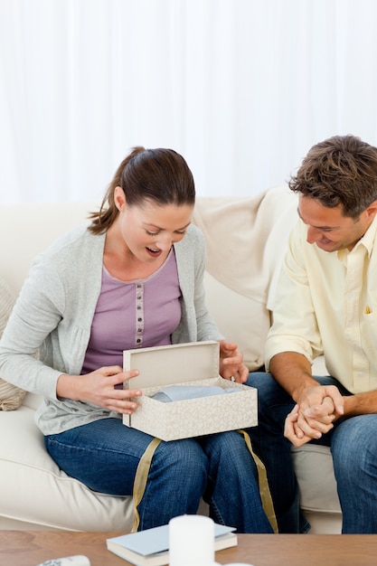 Photo amazed woman opening a present from his boyfriend on the sofa