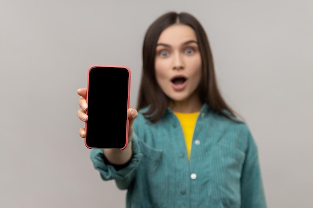 Amazed woman showing cell phone with empty display with copy space for advertisement