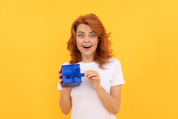 Amazed woman with present box on yellow background, boxing day